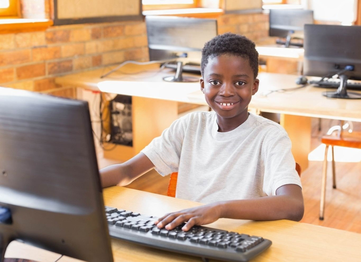 A boy smiling while using a computer in a school lab
